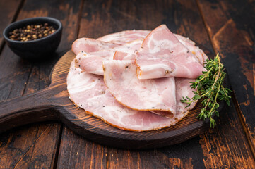 Slices of authentic Italian Pancetta Arrotolata served on a dark rustic cutting board with fresh thyme and peppercorns.
