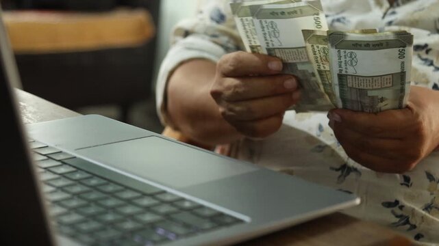 Indian Man Counting ₹500 Banknotes as Income While Working on Laptop