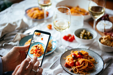 Taking a mobile photo of a table at a friendly dinner with pasta and wine at home.