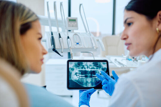 Dentist explaining dental X-ray images on a digital tablet to a patient during consultation at a modern dental clinic. Healthcare technology