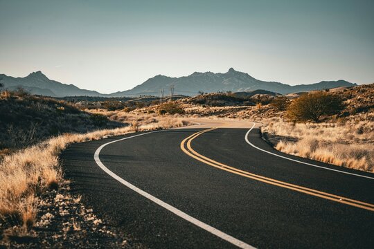 Curved asphalt road winding through a dry desert landscape with distant mountain ranges under a clear sky