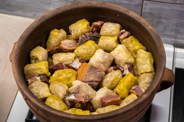 A traditional Serbian clay bowl filled with sarma (cabbage rolls) and dried meat, presented in an extreme close-up that highlights the texture and rustic authenticity of this classic Balkan dish.


