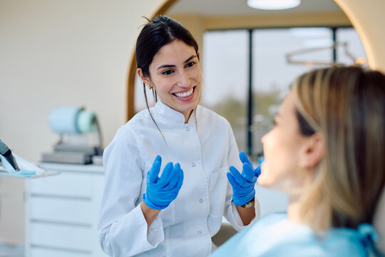 Female dentist wearing blue gloves and uniform, explaining treatment options to a smiling patient during a dental consultation