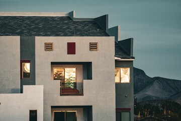 Modern residential building exterior with geometric design and mountain landscape in the background during sunset