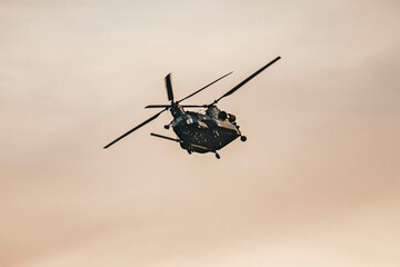 Military helicopter flying in the sky with rotor blades in motion against a cloudy backdrop, depicting aerial transport and defense operations
