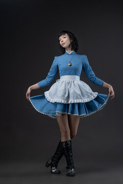 Costumed Gothic Alice: woman in blue Victorian dress with apron, Wonderland mood.