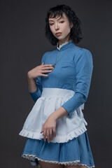Full-length photo of Gothic Alice in blue Victorian dress with apron on gray.