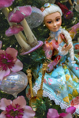 Whimsical vintage fairy doll on Christmas tree is surrounded by festive decorations, flowers and mushrooms