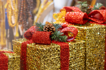 Festive gift boxes are shiny golden in color with red ribbon and decorations in form of pine cones in close-up