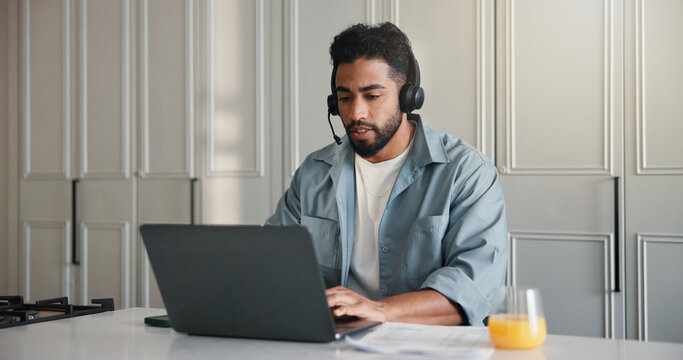 Headset, laptop and remote work with man in kitchen of home for startup planning or research. Computer, small business and typing with freelance employee at counter in apartment for online feedback