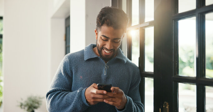 Window, typing and happy man with phone, browsing internet and check social media post. Message notification, texting and person in home with mobile app, online communication and reply to comment. - Powered by Adobe