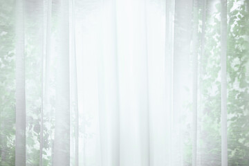 A beautiful scene of white window curtains with a natural backdrop of green leaves and soft, warm morning sunlight reflecting through the silk.