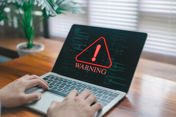 Laptop screen displaying a red digital warning alert with exclamation symbol over coding background, representing cybersecurity threat, system error, data risk, malware attack, and computer security