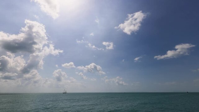 Tropical seascape timelapse showing boats on the horizon under a vivid blue sky with drifting white clouds and sunlight reflecting on calm turquoise water. Perfect for themes of relaxation, travel, a.