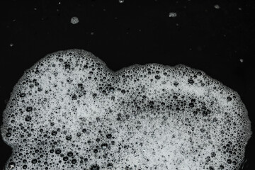 white soap foam texture with small and large air bubbles spread across the surface of the water