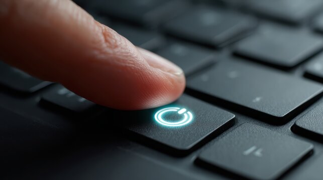 Finger pressing the power button on a laptop keyboard, close-up shot