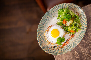 brunch dish featuring a sunny-side-up egg on toast or patty, accompanied by fresh green salad with parsley and carrots on a decorative plate.