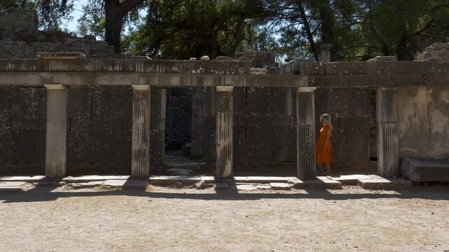 Footage of a woman in an orange dress walking among historical ruins.