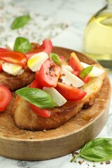Tasty bruschettas with mozzarella cheese, tomatoes and basil on white marble table, closeup