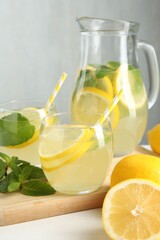 Fresh lemonade in glasses, jug, lemons and mint on white table, closeup