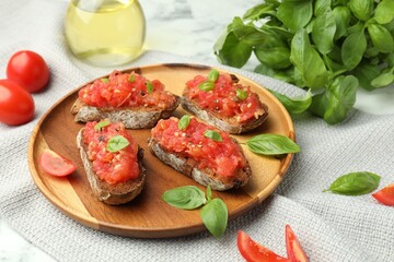 Tasty bruschettas with tomatoes and basil on white marble table, closeup