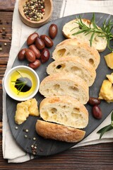 Pieces of fresh ciabatta, oil, olives, cheese, rosemary and peppercorns on wooden table, flat lay
