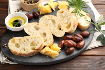 Pieces of fresh ciabatta, oil, olives, cheese, rosemary and peppercorns on wooden table, closeup