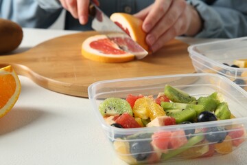 Making fruit salad. Woman cutting grapefruit at white table, closeup
