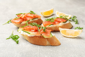 Tasty bruschettas with salmon, cream cheese, cucumber, arugula and lemon on grey table, closeup