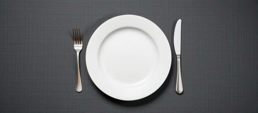 Empty plate with knife and fork on a textured dark surface. - Powered by Adobe