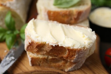 Slices of baguette with butter, basil and knife on wooden table, closeup