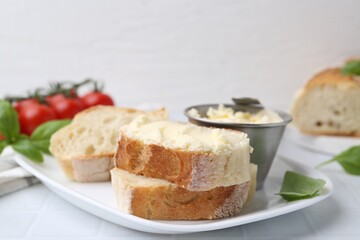 Slices of baguette with butter and basil on white tiled table, closeup. Space for text