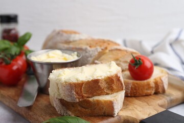 Cut baguette with butter, basil, tomatoes and knife on light table, closeup