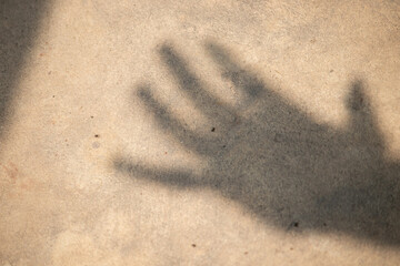 Abstract background: shadow of a human hand on a rough concrete texture, help or fear concept