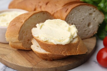 Cut baguette with butter, basil and tomatoes on white table, closeup