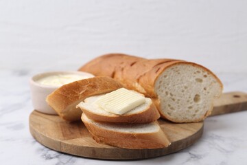 Cut baguette with butter on white marble table, closeup. Space for text