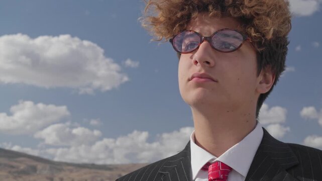 Portrait of a handsome, serious teenager in a business suit against a blue sky.