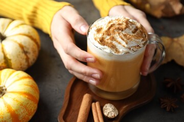 Woman holding tasty pumpkin latte with whipped cream at grey table, closeup