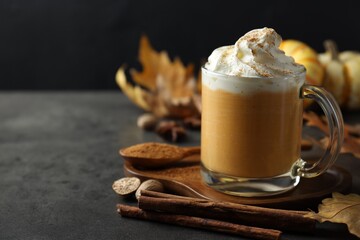 Tasty pumpkin latte with whipped cream in glass cup, spices and autumn decor on grey table, closeup. Space for text