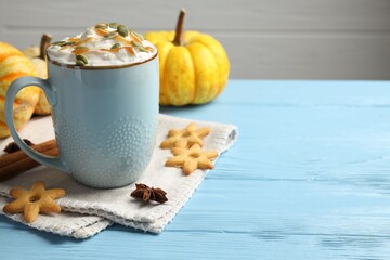 Tasty pumpkin latte with whipped cream in cup, spices and cookies on light blue wooden table, closeup. Space for text