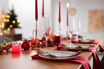Stylish Christmas table setting with plates, glasses and burning candles in room, closeup. Bokeh effect