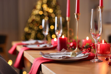 Stylish Christmas table setting with plates, glasses and burning candles in festive decorated room, closeup. Bokeh effect