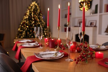 Stylish Christmas table setting with plates, glasses and burning candles in festive decorated room. Bokeh effect