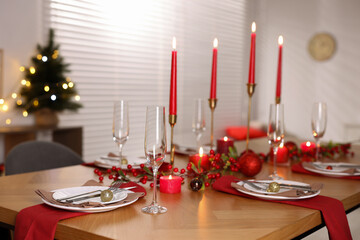 Stylish Christmas table setting with plates, glasses and burning candles in festive decorated room, closeup