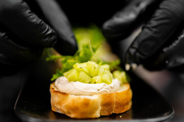 Professional chef preparing a fresh cucumber and cream cheese bruschetta in a restaurant kitchen setting.