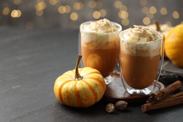 Tasty pumpkin latte with whipped cream, spices and fresh vegetable on black table against blurred lights, closeup. Space for text