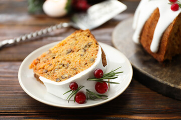 Piece of delicious Christmas cake with icing, cranberries and rosemary on wooden table, closeup