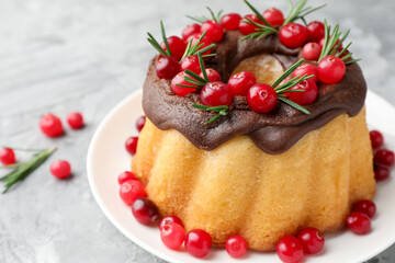 Delicious Christmas cake with chocolate glaze, cranberries and rosemary on light grey textured table, closeup