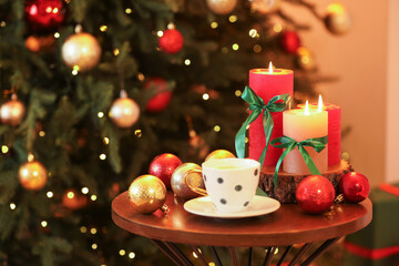 Burning candles, cup of coffee and festive decor on table near Christmas tree indoors, closeup. Space for text