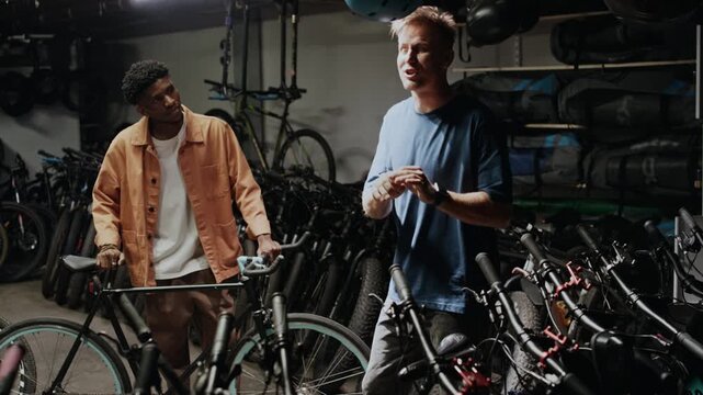 Young Caucasian seller working in bicycle shop, giving recommendations to Black male customer, helping him to choose bike